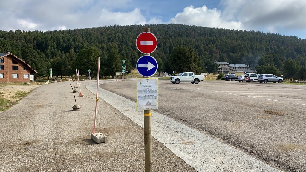 Pla obert de l'aparcament del Refugi Cap del Rec, a la base de l'estació de nòrdic de Lles, amb un cartell que indica la prohibició de circular als vehicles i uns horaris dels busos que van a Pollineres. Imatge de l'1 de setembre de 2021. (Horitzontal)
