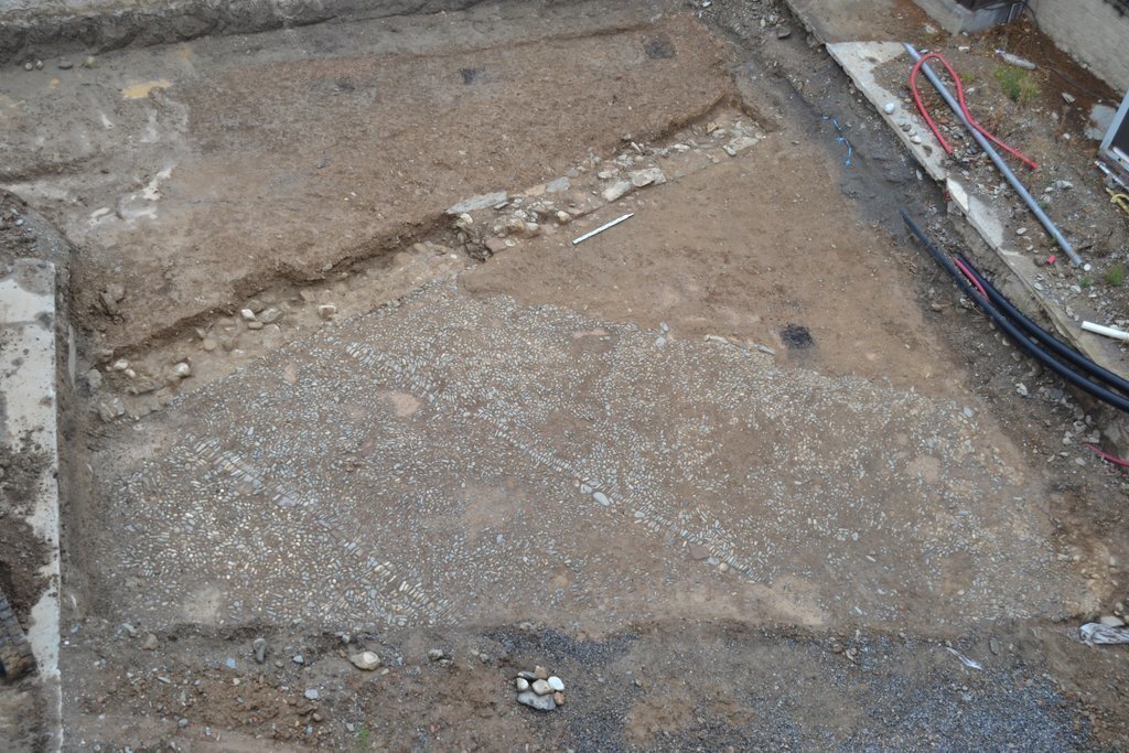 Pla obert de l'àrea excavada al jaciment del pati de les Monges de la Seu d'Urgell amb la gran plaça pavimentada amb còdols delimitada per la muralla baix medieval descoberta en les tasques de delimitació de la zona, el 9 de setembre de 2021 (Horitzontal)