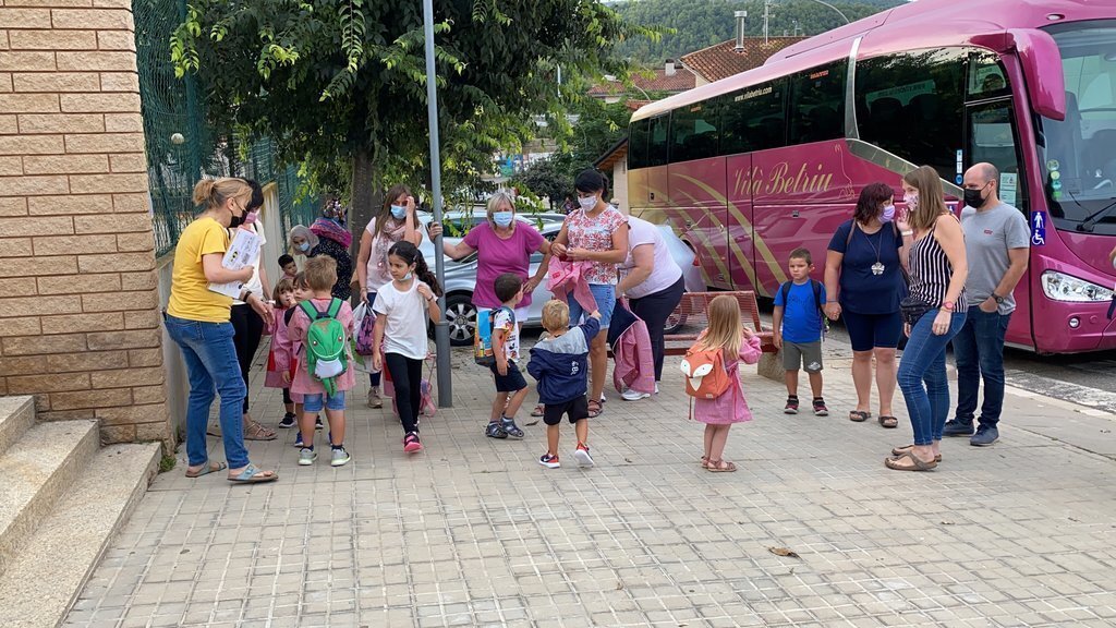 Pla obert d'un grup d'alumnes de l'Institut Escola d'Oliana (Alt Urgell) esperant, amb els seus pares, a entrar a l'escola el primer dia de curs, on es veu una part d'un dels autobusos que porta escolars. Imatge del 13 de setembre de 2021. (Horitzontal)