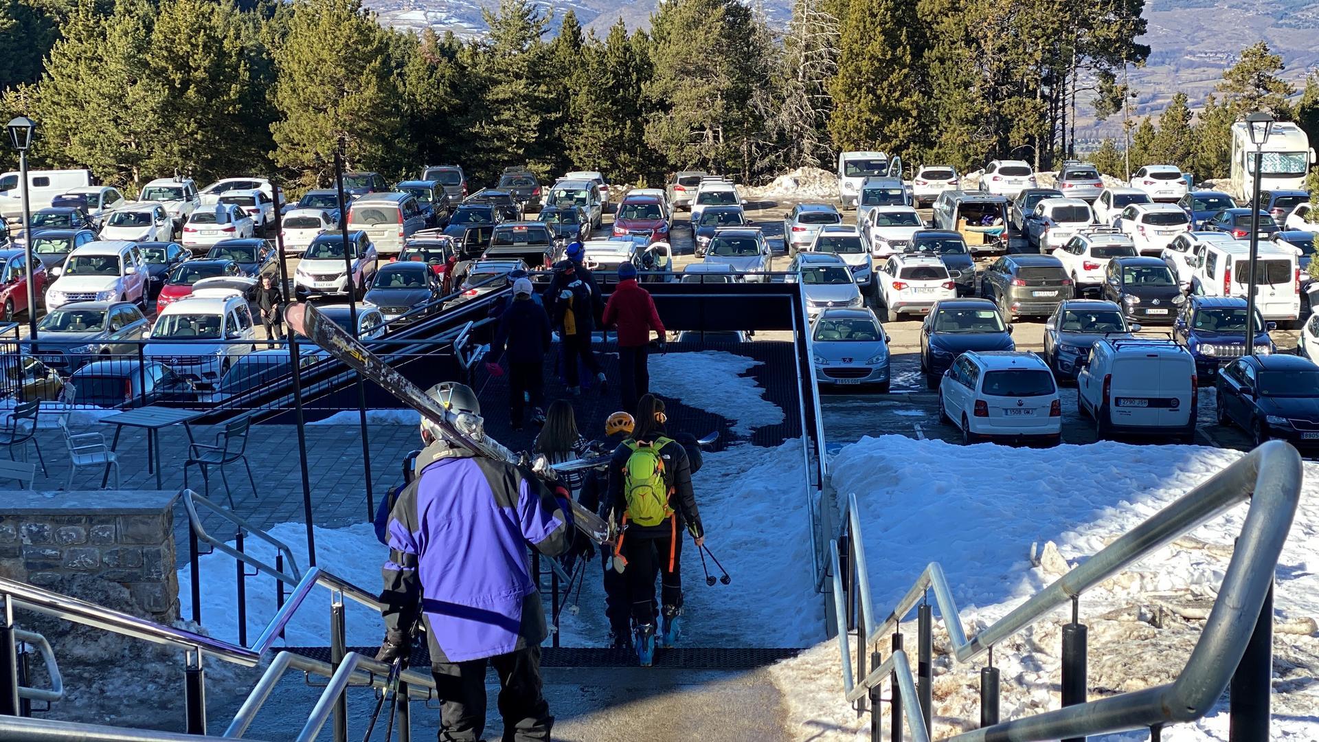 Pla sencer de diversos esquiadors accedint a l'aparcament de l'estació de Masella (Cerdanya) on es veu una part dels vehicles estacionats. Imatge publicada el 21 de desembre de 2021. (Horitzontal)